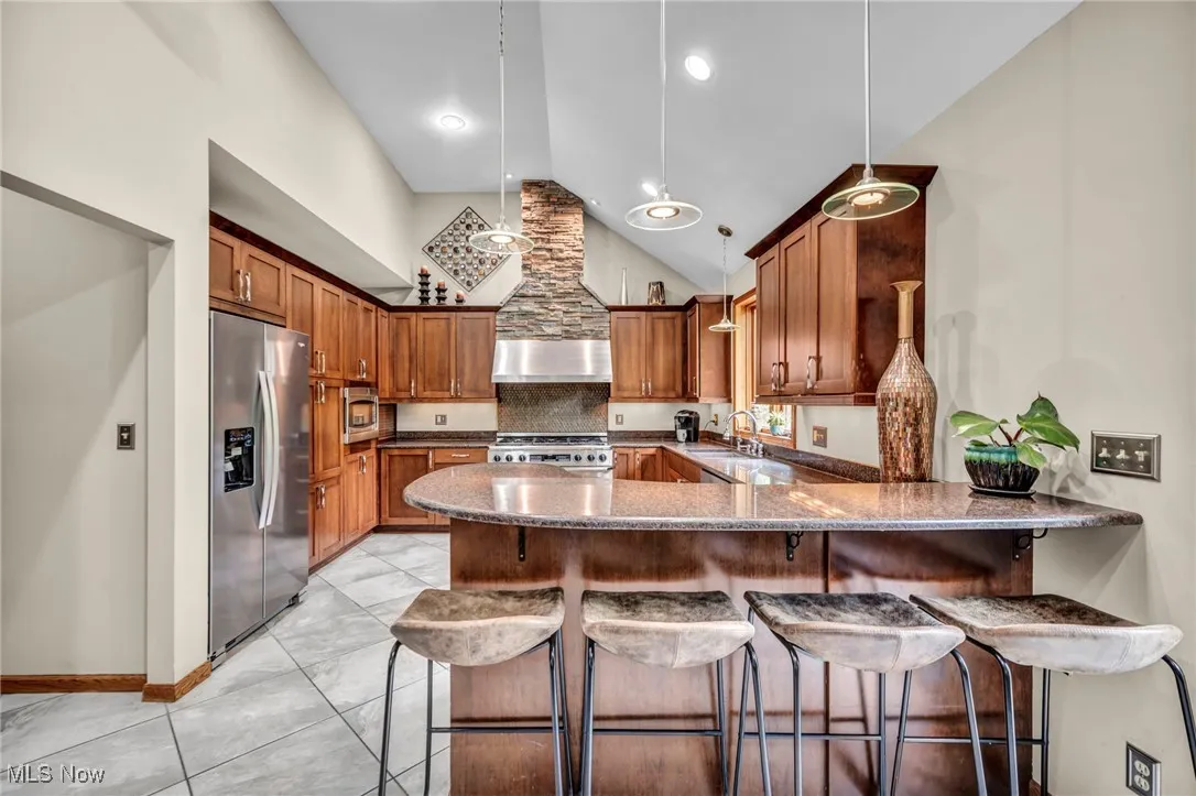 Kitchen with appliances with stainless steel finishes, high vaulted ceiling, breakfast bar, exhaust hood, and wood cabinetry