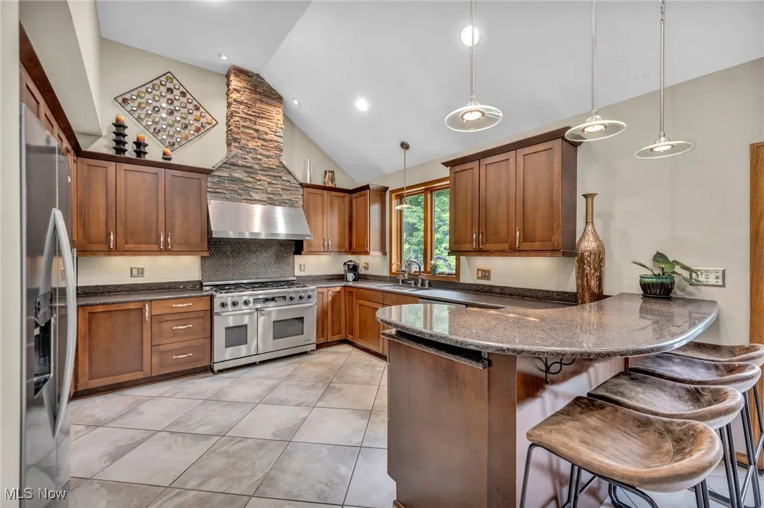 Kitchen featuring stainless steel appliances, high vaulted ceiling, brick exhaust hood, a breakfast bar and  backsplash