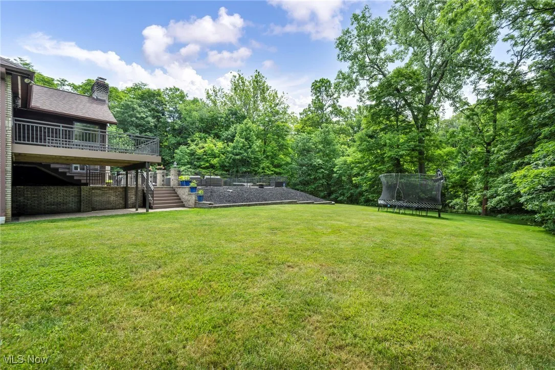 Side of home View of grassy yard with stairs, a trampoline, and a deck