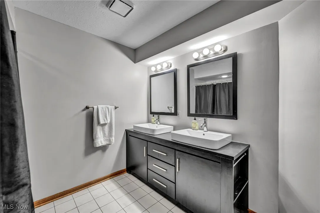 Full bathroom lower featuring double vanity, tile  flooring, and a textured ceiling