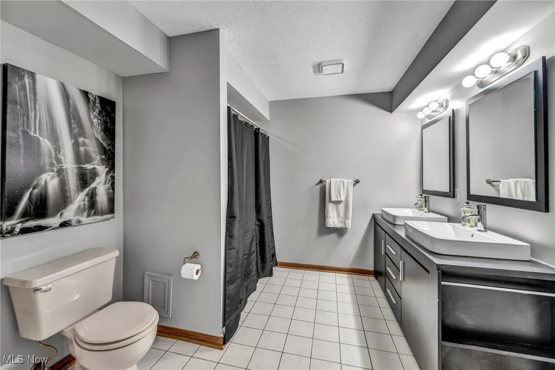 Full bath with double vanity, a textured ceiling, tile patterned floors, and a shower with curtain