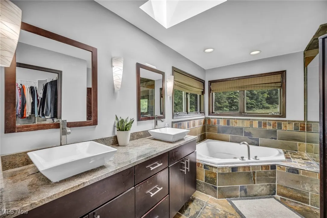 Primary in suite bathroom with a bath, double vanity, a skylight, stone finish floors, and recessed lighting