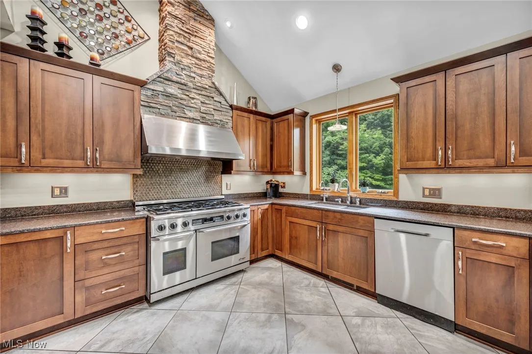 Kitchen featuring stainless steel appliances,  range hood, granite countertops, wood cabinets, and decorative backsplash
