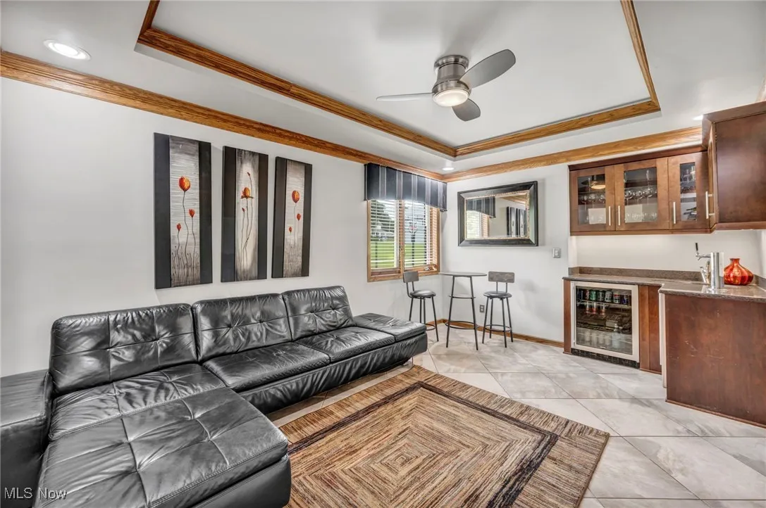 Lounge area with a tray ceiling, beverage cooler, wet bar, ornamental molding,
