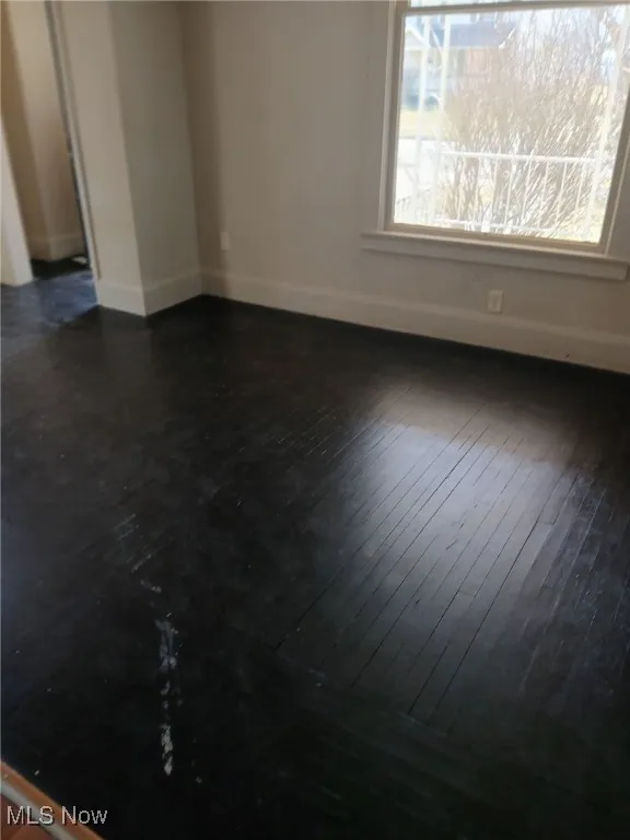 Spare room featuring baseboards and dark wood-style flooring