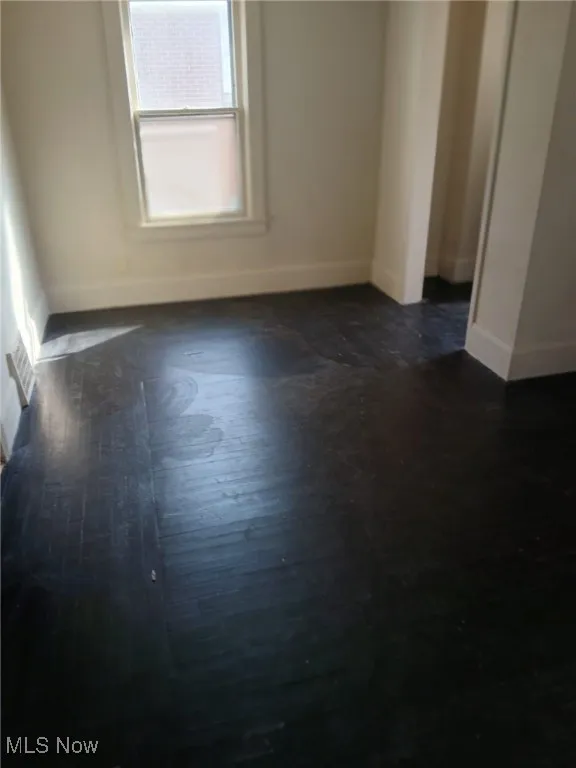 Spare room featuring baseboards and dark wood-style flooring