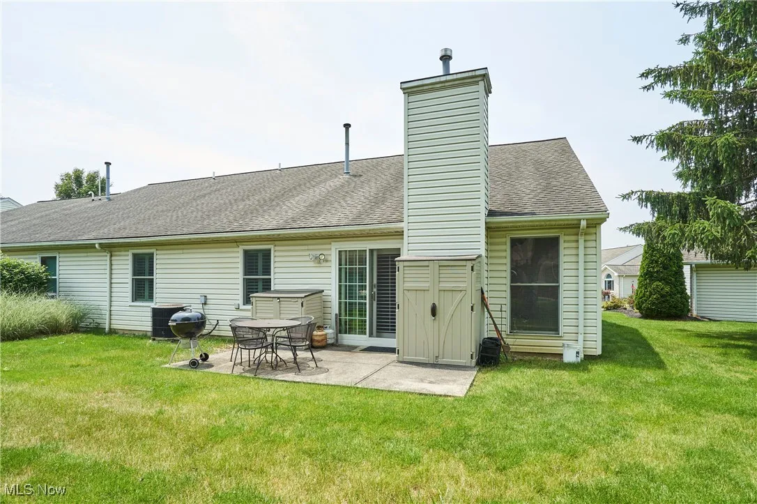 Rear view of property featuring a patio area, a yard, a chimney, and a shingled roof