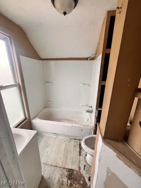 Bathroom with vaulted ceiling, shower / washtub combination, and wood finished floors