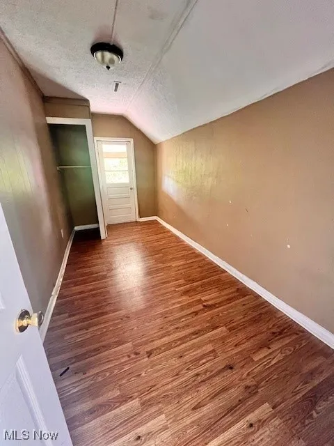 Additional living space with vaulted ceiling, wood finished floors, and a textured ceiling