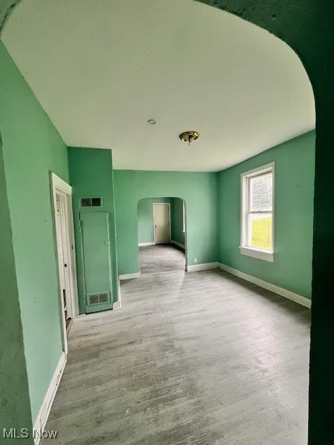 Unfurnished room featuring arched walkways and wood finished floors