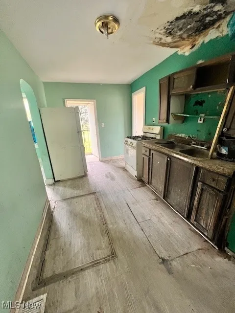 Kitchen with white appliances, light wood finished floors, dark countertops, and arched walkways
