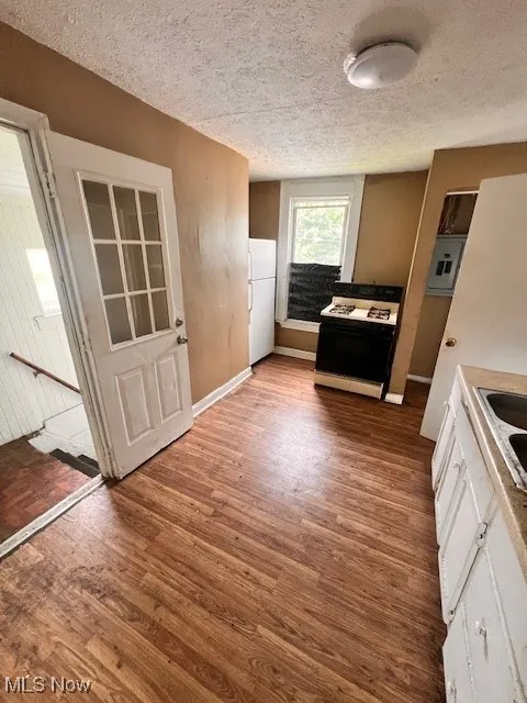 Kitchen featuring white appliances, a textured ceiling, light wood finished floors, and white cabinetry