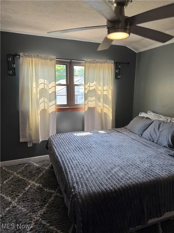 Bedroom with a textured ceiling, a ceiling fan, vaulted ceiling, and carpet floors