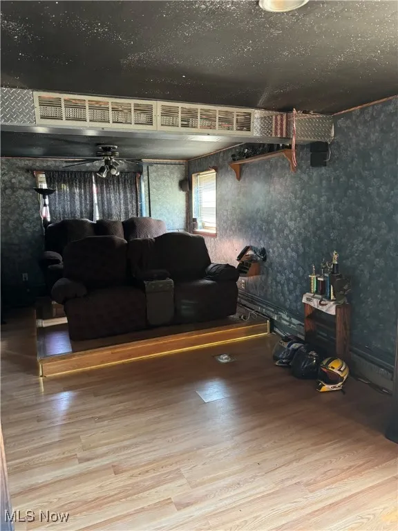 Living area featuring wood finished floors, a ceiling fan, and wallpapered walls