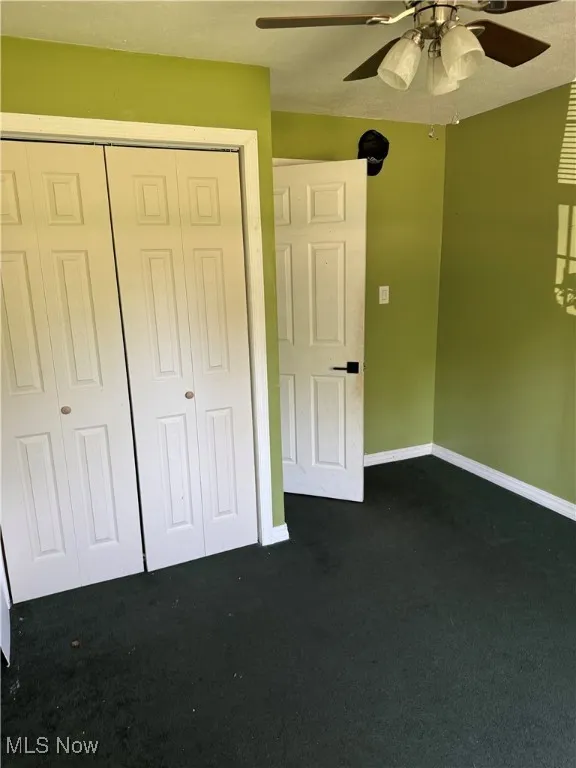 Unfurnished bedroom with dark colored carpet, a closet, and ceiling fan