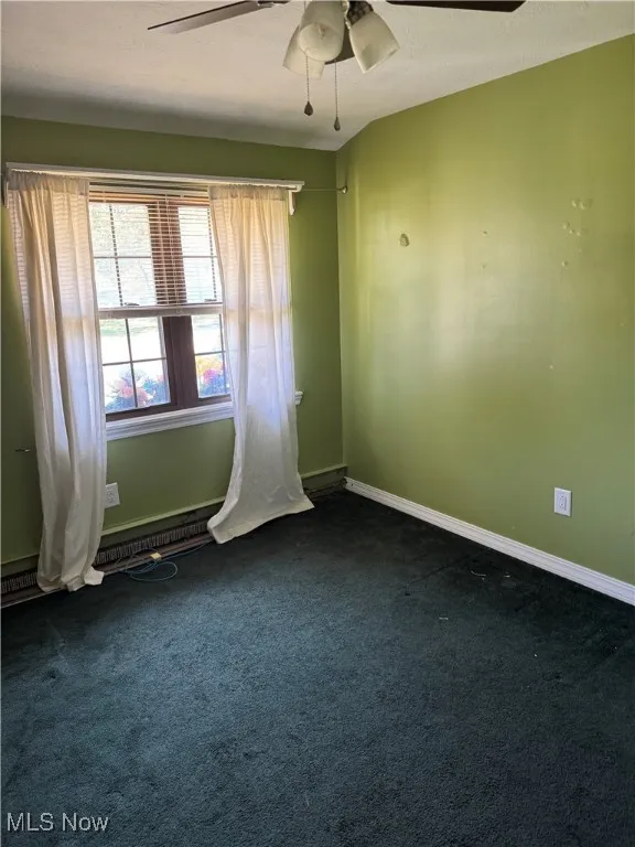 Empty room featuring ceiling fan and dark colored carpet