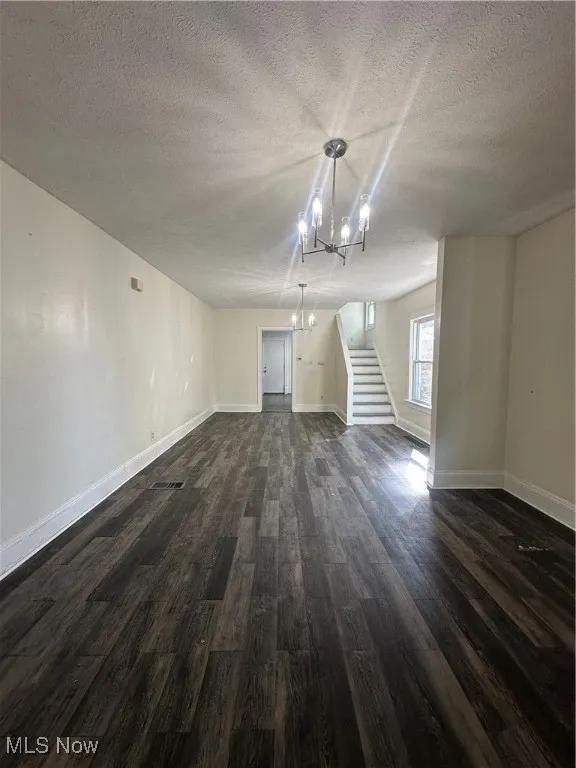 Unfurnished living room with a chandelier, a textured ceiling, dark wood-style floors, and stairs