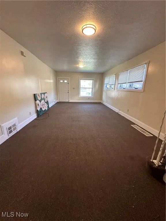 Spare room with a textured ceiling and dark colored carpet