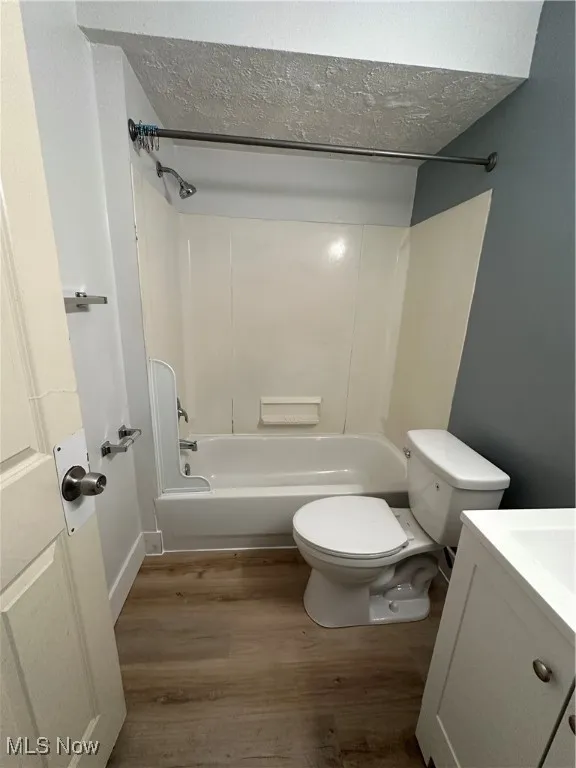 Full bath with vanity, wood finished floors, shower / tub combination, and a textured ceiling