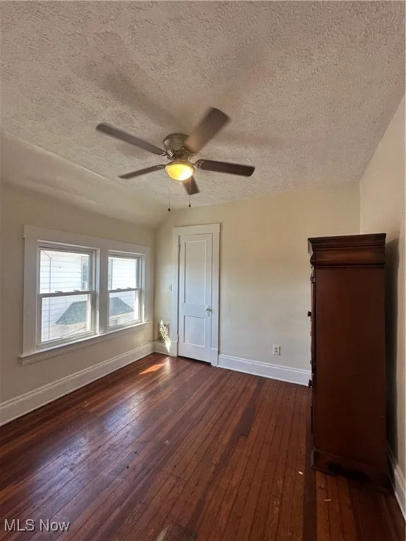 Unfurnished bedroom with dark wood-style flooring, a textured ceiling, and ceiling fan