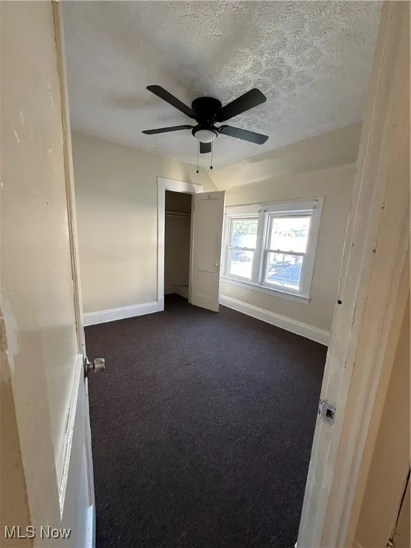 Unfurnished bedroom featuring dark carpet, a textured ceiling, ceiling fan, and a closet