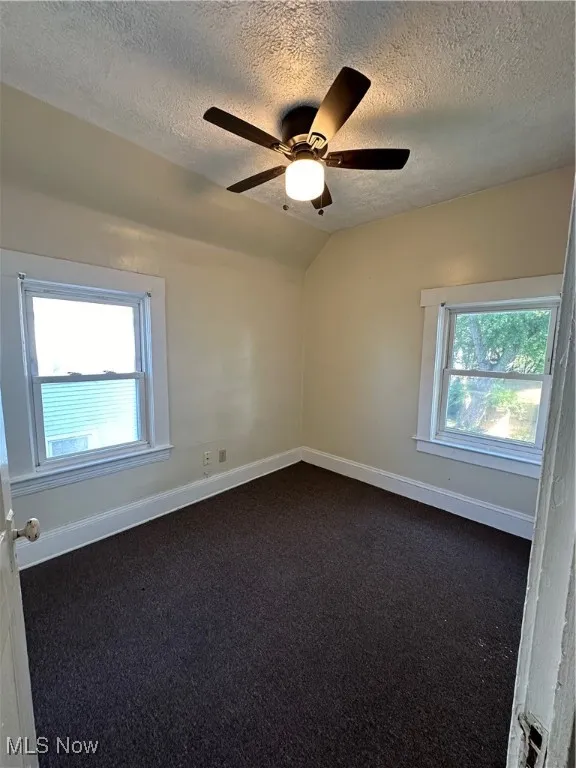 Unfurnished room featuring a textured ceiling, dark carpet, lofted ceiling, and ceiling fan
