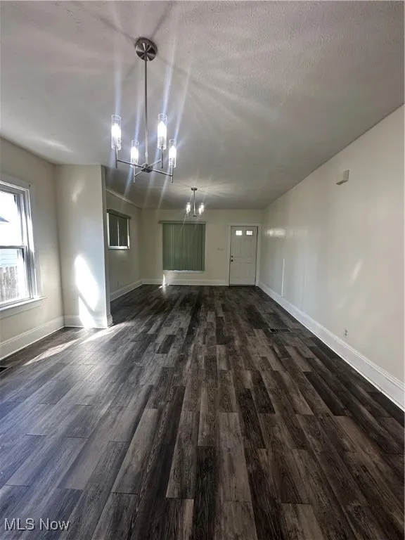 Unfurnished living room featuring a chandelier, dark wood-style floors, and a textured ceiling