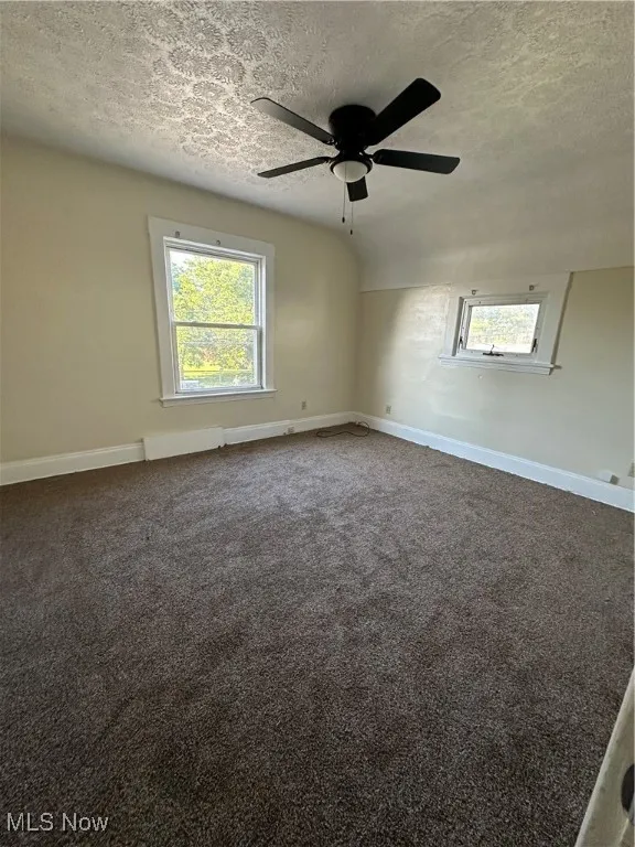 Unfurnished room featuring a textured ceiling, ceiling fan, healthy amount of natural light, and dark carpet