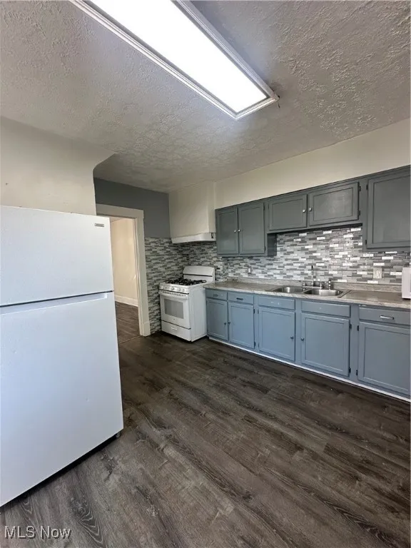 Kitchen with fridge, range with gas stovetop, a textured ceiling, dark wood finished floors, and decorative backsplash