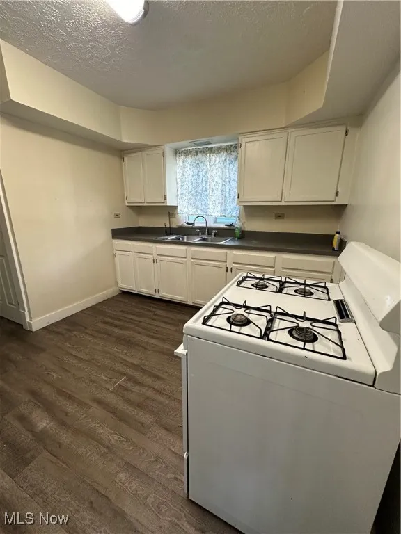 Kitchen with stove, dark countertops, dark wood-style floors, white cabinets, and a textured ceiling