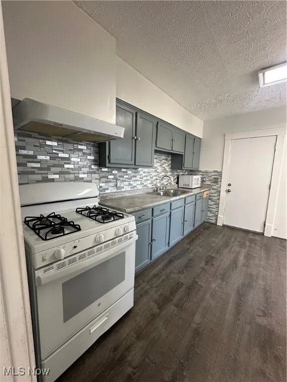Kitchen featuring stove, a textured ceiling, dark wood-style floors, gray cabinets, and decorative backsplash