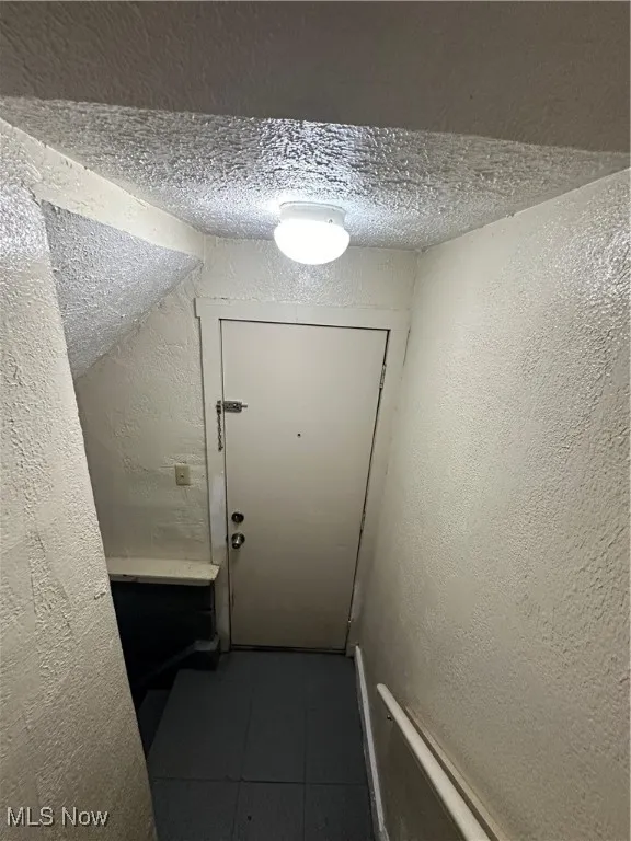 Doorway featuring a textured wall, a textured ceiling, and tile patterned floors