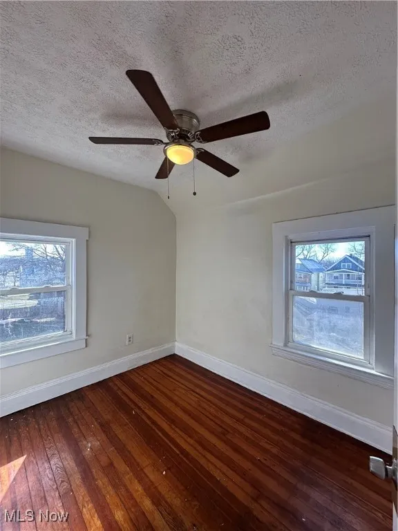 Spare room featuring a textured ceiling, plenty of natural light, hardwood / wood-style floors, a ceiling fan, and vaulted ceiling