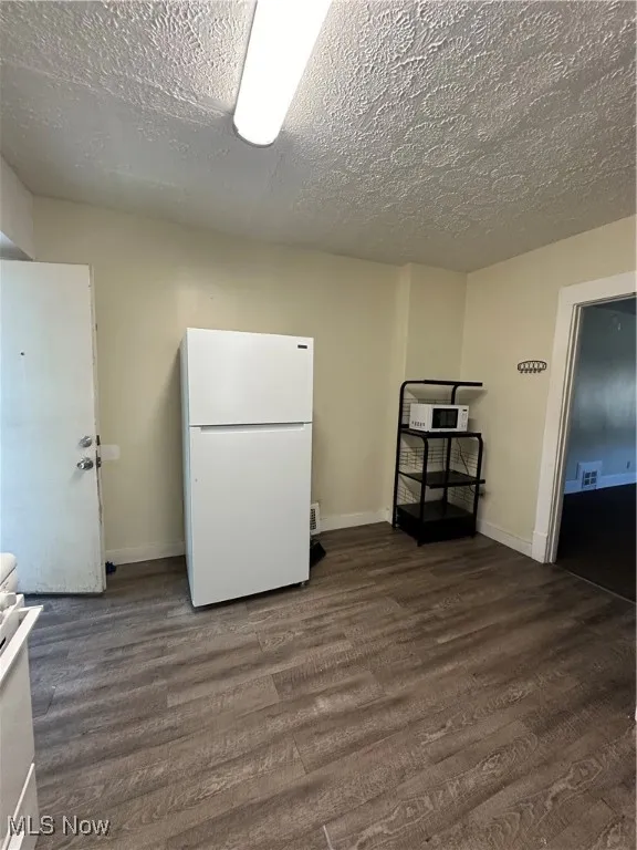 Kitchen with fridge, dark wood finished floors, a textured ceiling, and range