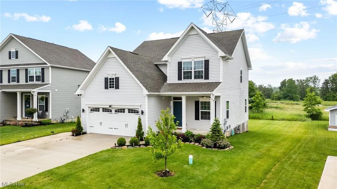 Traditional home featuring covered porch, roof with shingles, driveway, a garage, and a front yard