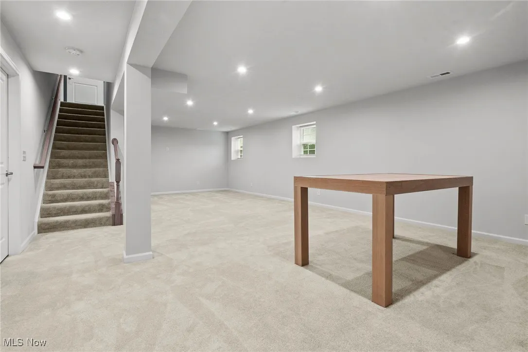 Below grade area featuring light carpet, recessed lighting, and stairs