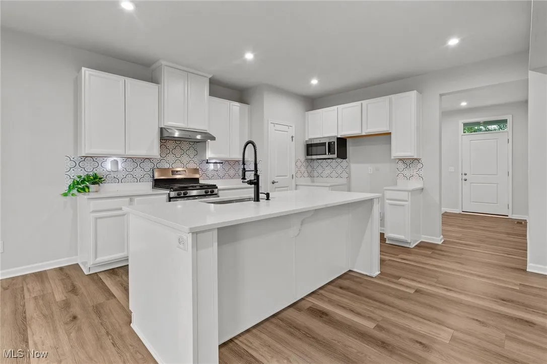 Kitchen featuring stainless steel appliances, an island with sink, white cabinets, tasteful backsplash, and light wood-style floors