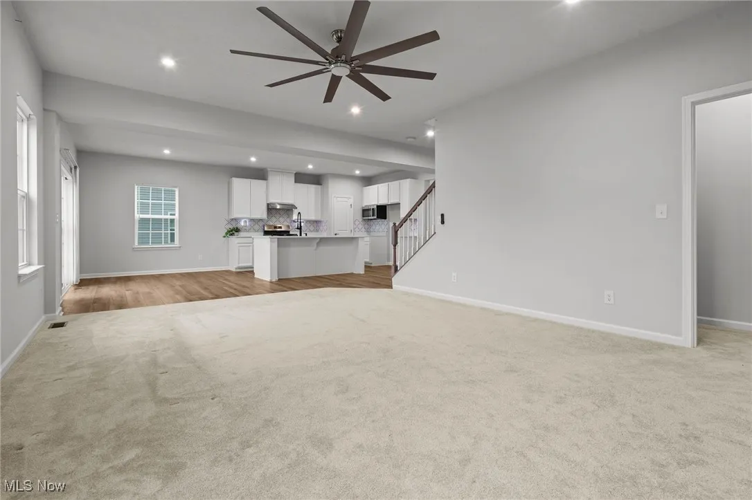 Unfurnished living room featuring light carpet, a ceiling fan, recessed lighting, and stairway