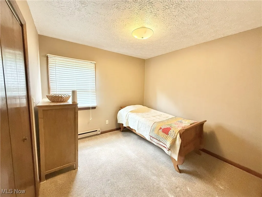 Carpeted bedroom featuring a baseboard radiator, a closet, and a textured ceiling