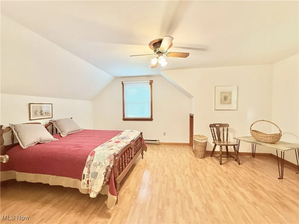 Bedroom featuring light wood-style flooring, a baseboard radiator, lofted ceiling, and a ceiling fan
