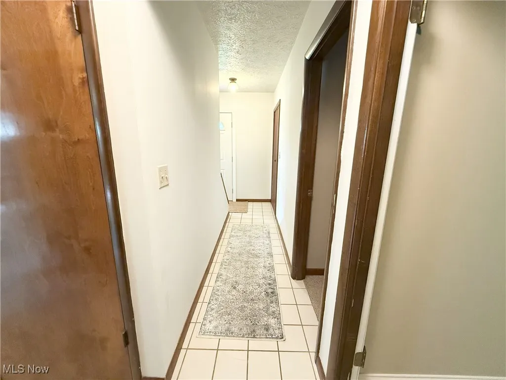 Corridor with a textured ceiling and light tile patterned floors