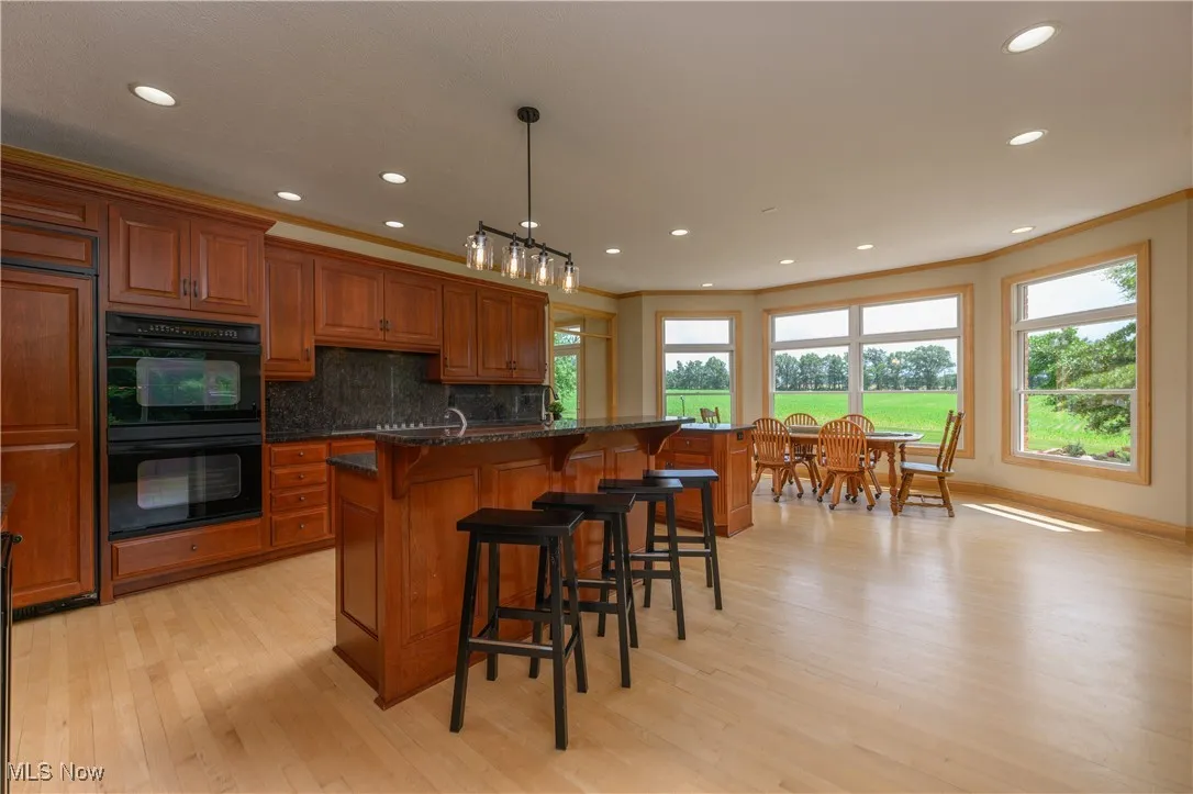Kitchen with brown cabinets, light wood finished floors, a kitchen breakfast bar, recessed lighting, and tasteful backsplash