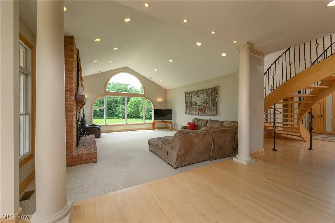 Living room with decorative columns, wood finished floors, vaulted ceiling, a fireplace, and stairway