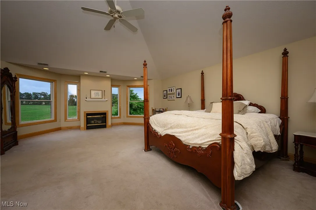 Bedroom with light carpet, lofted ceiling, a glass covered fireplace, a ceiling fan, and recessed lighting