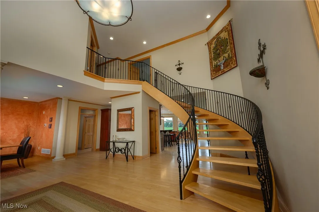 Staircase with wood finished floors, recessed lighting, a towering ceiling, decorative columns, and ornamental molding