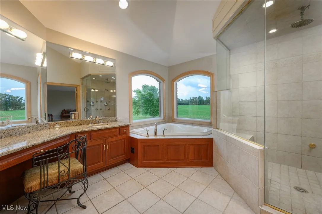 Full bath with a shower stall, tile patterned floors, vanity, a garden tub, and vaulted ceiling