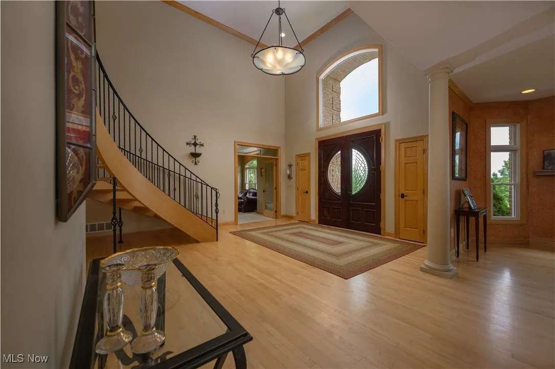 Foyer entrance with wood finished floors, stairway, decorative columns, ornamental molding, and a high ceiling