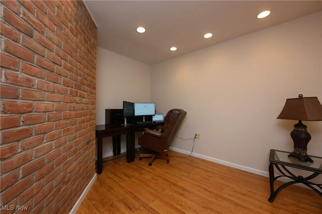 Office space with light wood finished floors, brick wall, and recessed lighting
