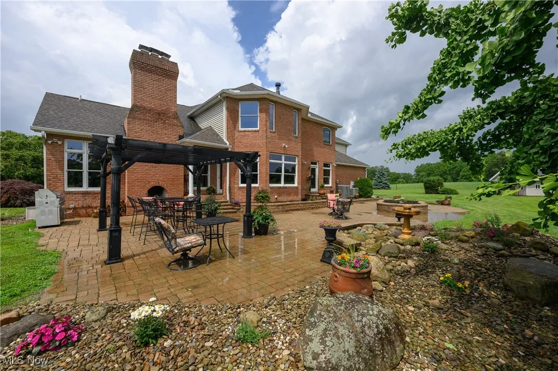 Rear view of house with brick siding, a patio area, a chimney, roof with shingles, and a fire pit