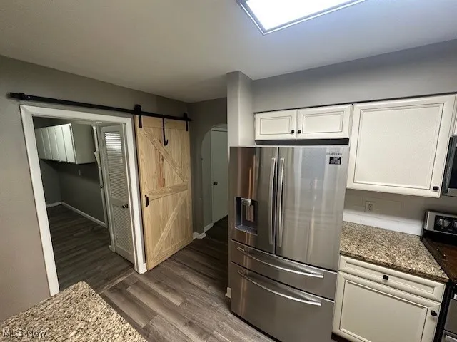 Kitchen featuring fridge, stove, dark wood-style floors, white cabinetry, and stone counters